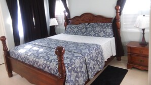 A bedroom with a wooden bed, dark curtains, a white air conditioning unit, and a nightstand with a lamp. - OCHO RIOS Jamaica Paradise House 2 (St Ann's Bay)