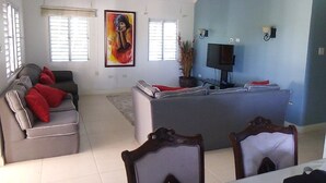 A spacious living area with a grey sofa, red cushions, a large painting, a flat-screen TV, and a ceiling fan. - OCHO RIOS Jamaica Paradise House 2 (St Ann's Bay)