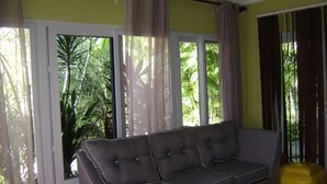 A living room with a grey sofa, a yellow bean bag, and a window with curtains. - OCHO RIOS Jamaica Paradise House 2 (St Ann's Bay)