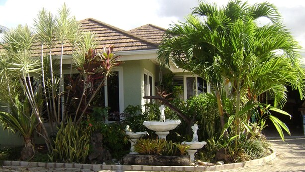 A house with a tiled roof, a garden with various plants, and a white fountain. - OCHO RIOS Jamaica Paradise House 2 (St Ann's Bay)