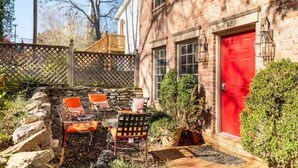 A brick building with a red door, outdoor seating with orange cushions, and a stone wall. - BEST LOCATION: Historic Shepherdstown Getaway (Shepherdstown)