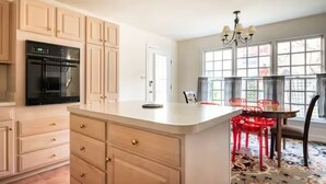 A kitchen with wooden cabinets, a built-in oven, and a dining area with a table and chairs. - BEST LOCATION: Historic Shepherdstown Getaway (Shepherdstown)