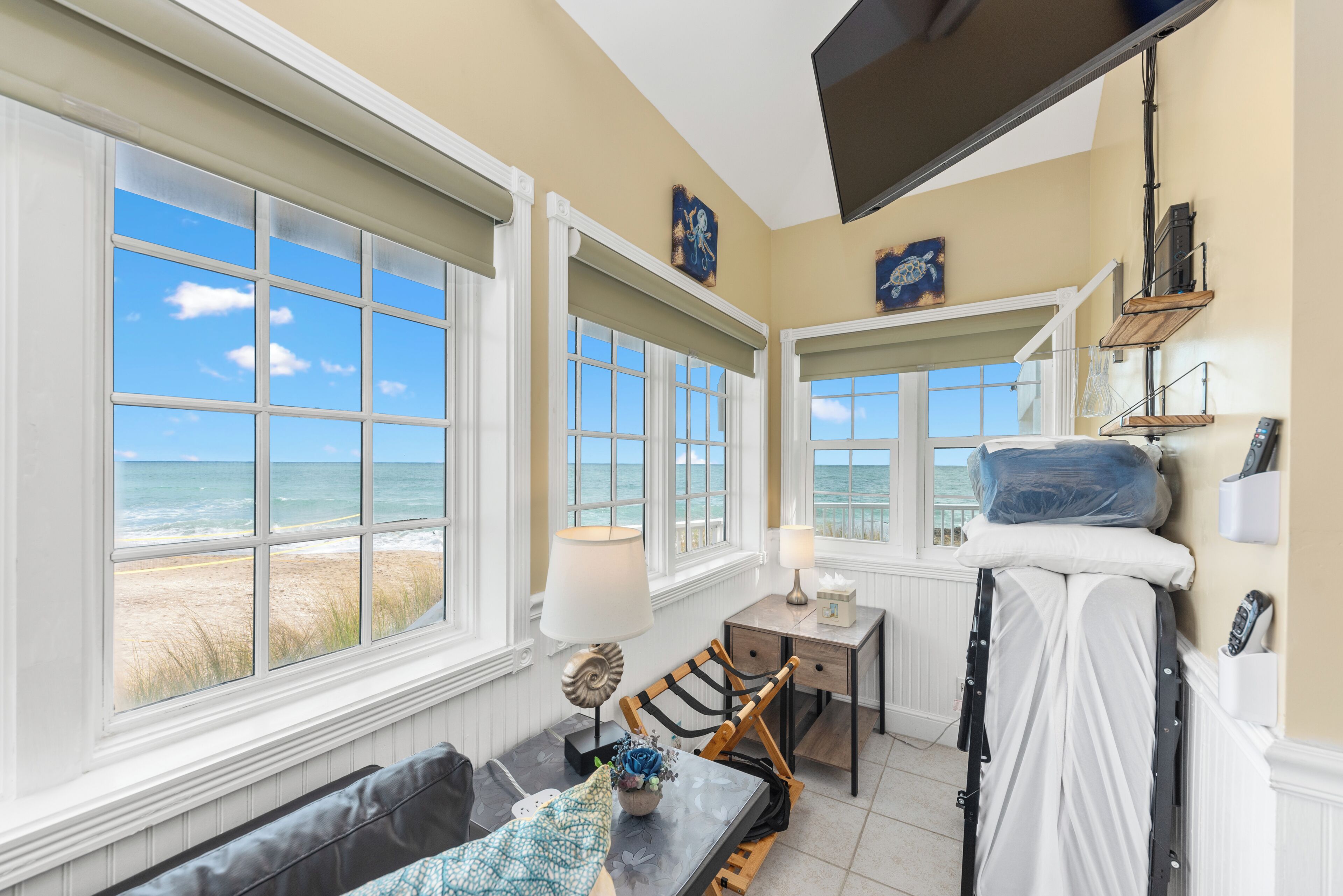 A room with a view of the beach, a bed, a table with a lamp, and a chair.