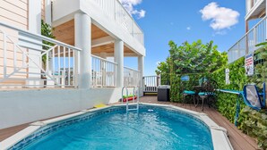 A swimming pool with a wooden deck, a white railing, and a covered area with chairs. - 3 Florida side-by-side Beach Houses; Sleeps 50+. Pools, Hot Tubs, Docks ON Beach (Stuart)
