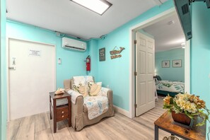 A room with teal walls, a bed with a floral bedspread, a chair with a blanket, a small table with a vase, and a door with a sign. - 3 Florida side-by-side Beach Houses; Sleeps 50+. Pools, Hot Tubs, Docks ON Beach (Stuart)