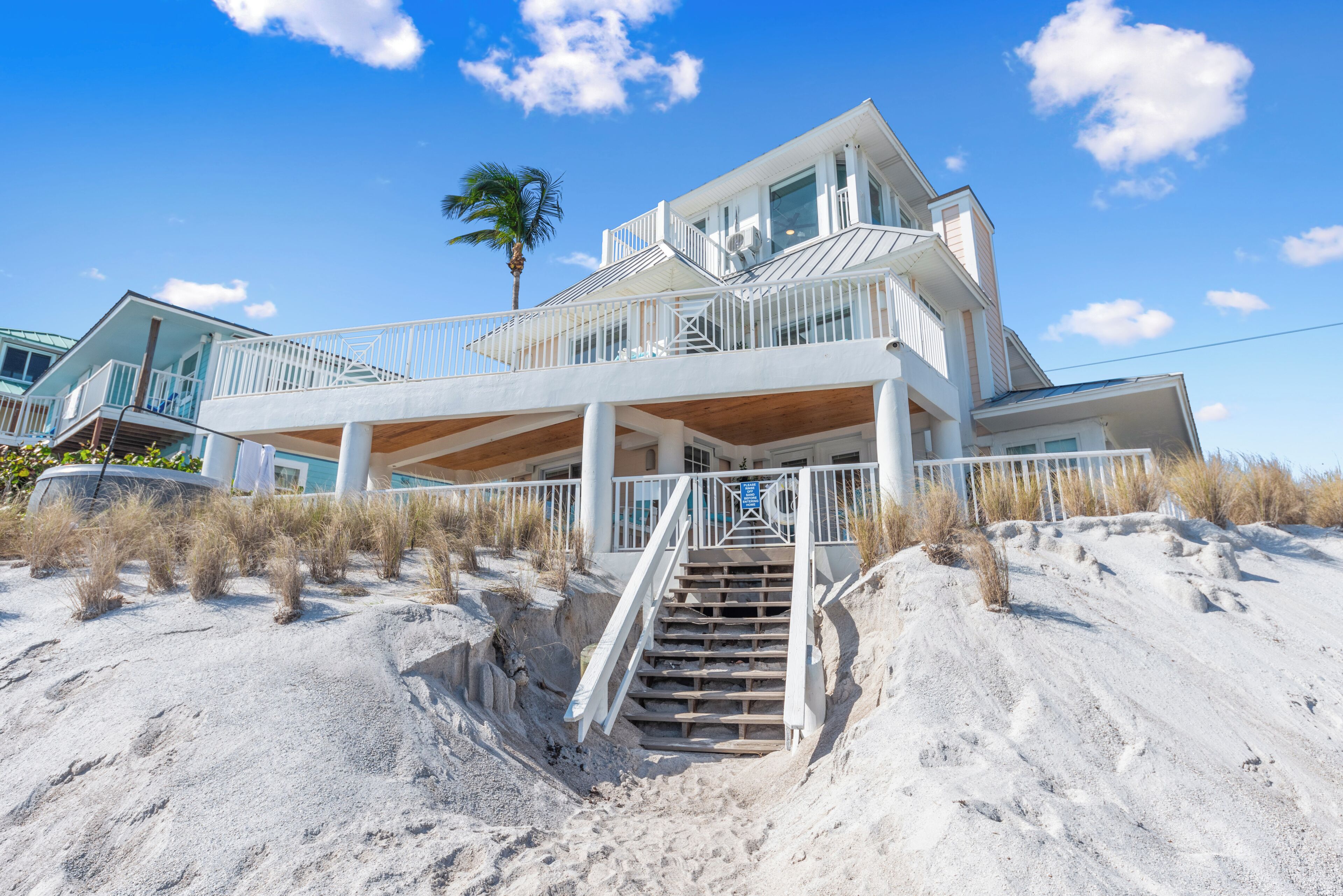 A beachfront property with a multi-level structure, including a balcony and a staircase leading to the beach.