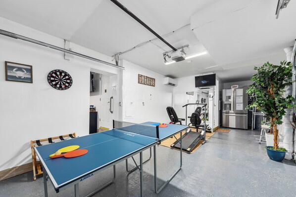 A ping pong table with paddles, a dartboard, and a wall-mounted projector.