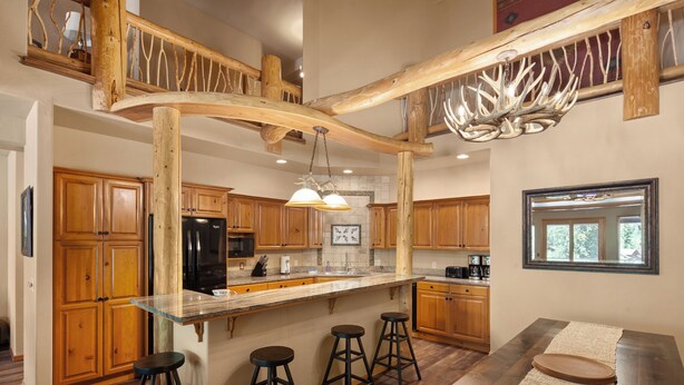 Une cuisine spacieuse avec des meubles en bois, un grand îlot central doté de tabourets et un plafond au style rustique.