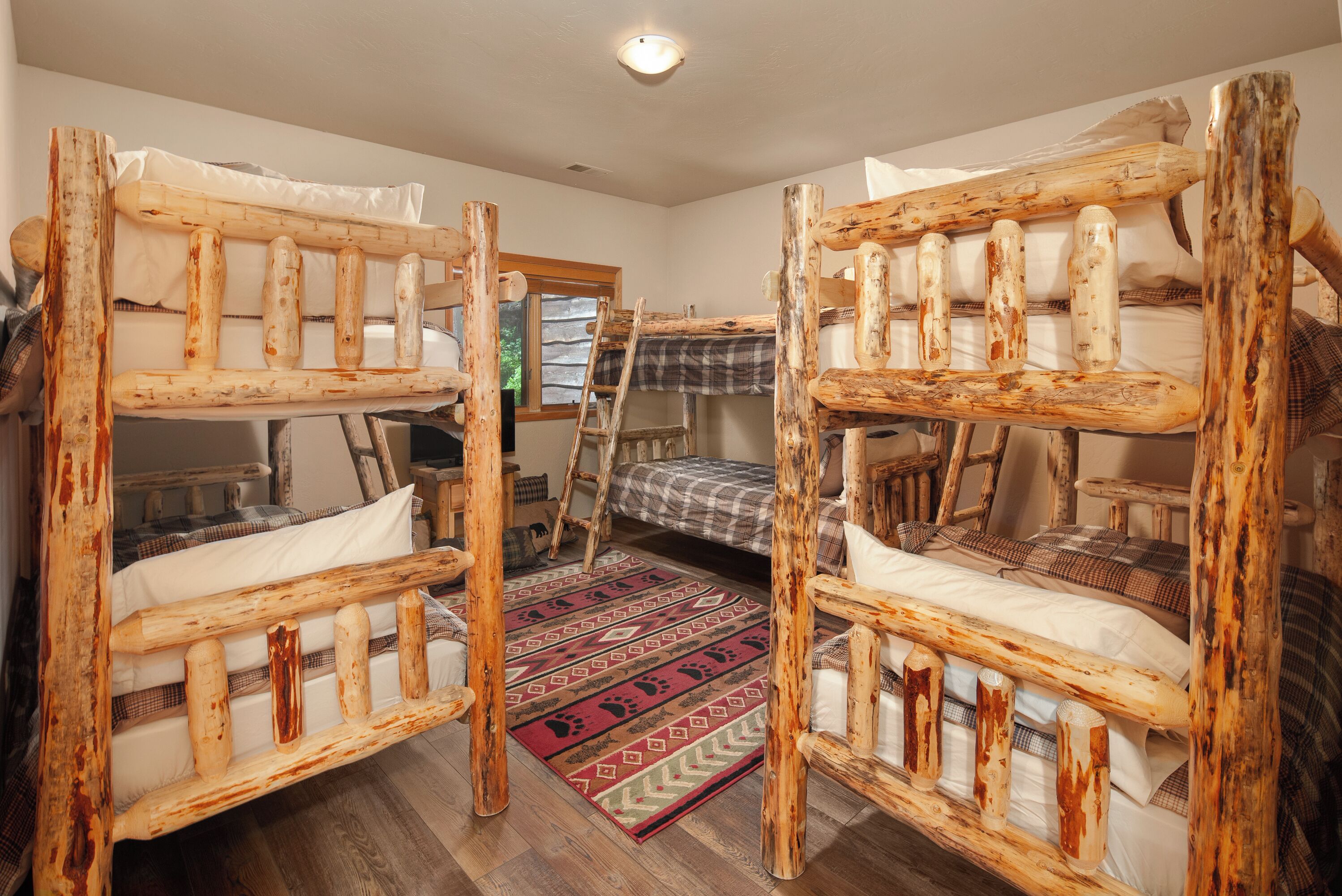 A rustic room with two bunk beds made of wood, a plaid blanket, and a red patterned rug.