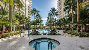 A pool area surrounded by palm trees and a multi-story building with balconies.