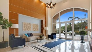 A spacious lobby with a modern design, featuring a large sofa, armchairs, and a coffee table. There is a large window offering a view of the outside.