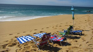Een strand met meerdere ligstoelen en parasols, een zandstrand en de oceaan op de achtergrond.