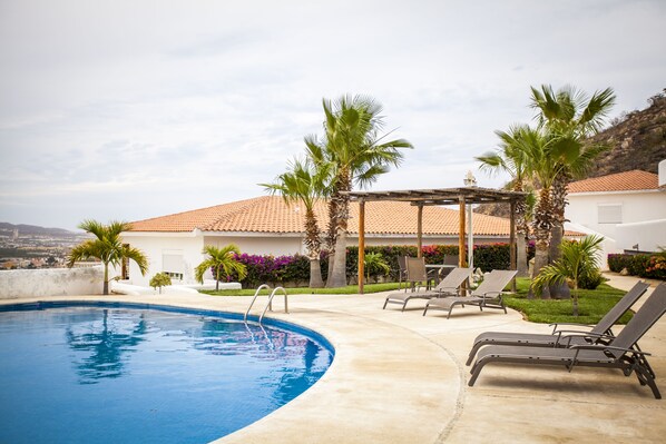 A swimming pool with lounge chairs, palm trees, and a building with a tiled roof. - Luxury Pedregal condo overlooking Cabo San Lucas! (Cabo San Lucas)