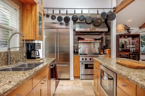 Una cocina moderna con encimeras de granito, electrodomésticos de acero inoxidable y un colgador para ollas.
