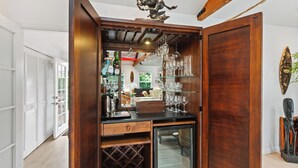 Un coin bar en bois, avec des étagères remplies de verres et de bouteilles, un réfrigérateur à vin et un élément décoratif au plafond.