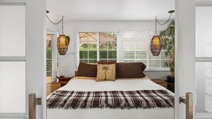 A bedroom with a bed, two hanging lamps, a window with blinds, and a plant. - Plantation Beach Cottage - Historic Encinitas Walking District (Encinitas)