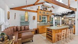 Un vaste espace de vie comprenant un grand canapé marron, des meubles en bois et une cuisine dotée d’un îlot central.
