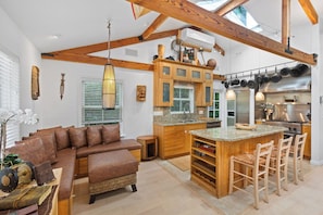 A spacious living area with a large brown sofa, wooden cabinets, and a kitchen with a central island.