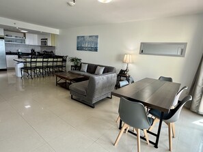 A modern living area with a sofa, coffee table, dining table, chairs, a lamp, and a painting on the wall.