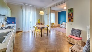 Une cuisine moderne avec un coin repas, un salon doté d’un canapé et un tableau coloré accroché au mur.