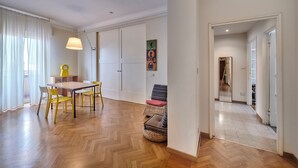 Une pièce spacieuse dotée d’un parquet en bois disposé en chevrons, d’une table à manger avec des chaises, d’une lampe et d’un tableau accroché au mur.
