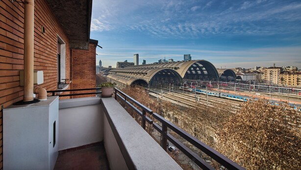 Un balcon avec vue sur une gare et sur le paysage urbain.