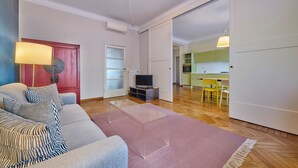 Un salon avec un canapé, un téléviseur et une cuisine visible à travers une porte ouverte.