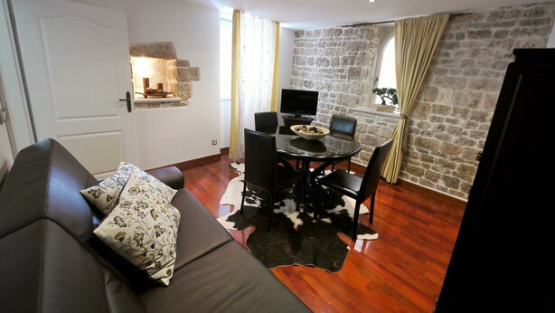 Een woonkamer met een bank, een eettafel met stoelen, een televisie en een stenen muur.
