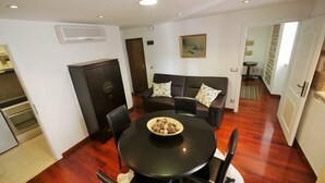 Een eetgedeelte met een ronde tafel, stoelen, een donker kast, een bank met gestreepte kussens en een schilderij aan de muur.