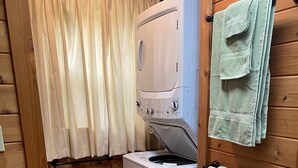 Een wasruimte met een voorlader wasmachine, houten wanden, een gordijn en handdoeken aan een rek.
