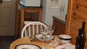 Een houten interieur met een eettafel gedekt voor twee personen, een magnetron en een koelkast.