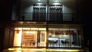 The exterior of the Fondness Hotel with a prominent illuminated sign, large windows, and a visible entrance area with seating. - Fondness Hotel (Takua Pa)