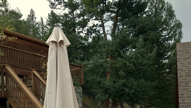 Een houten terras met buitenmeubilair, waaronder een tafel en stoelen, en een overdekt gedeelte met een witte parasol.