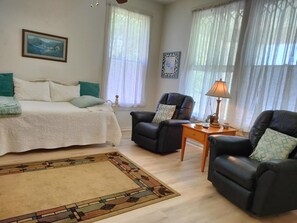 A bedroom with a bed, two chairs, a nightstand, and a lamp.