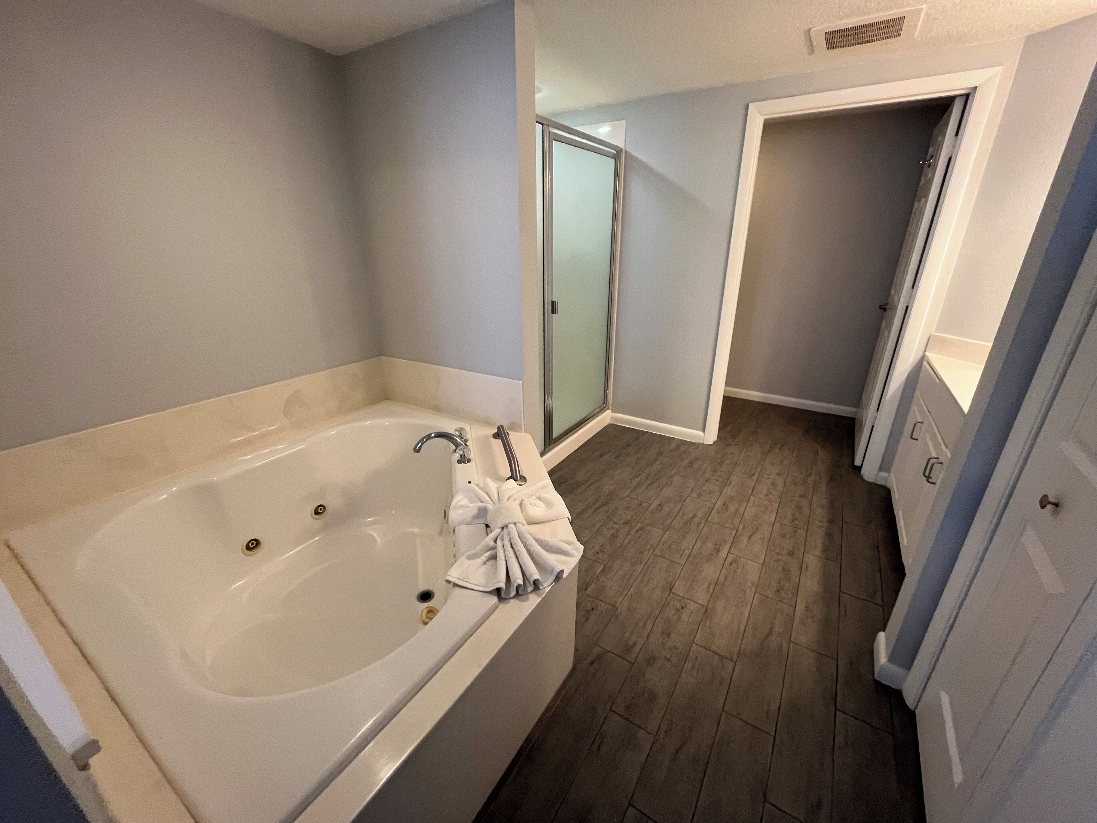 A bathroom with a large bathtub, a glass shower enclosure, and wooden flooring.