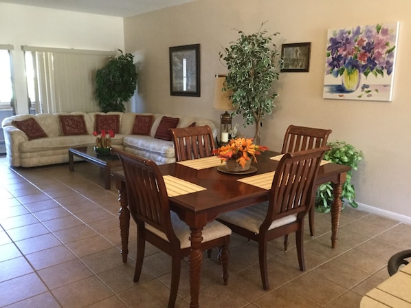 A dining area with a wooden table and chairs, a sofa, and a potted plant.