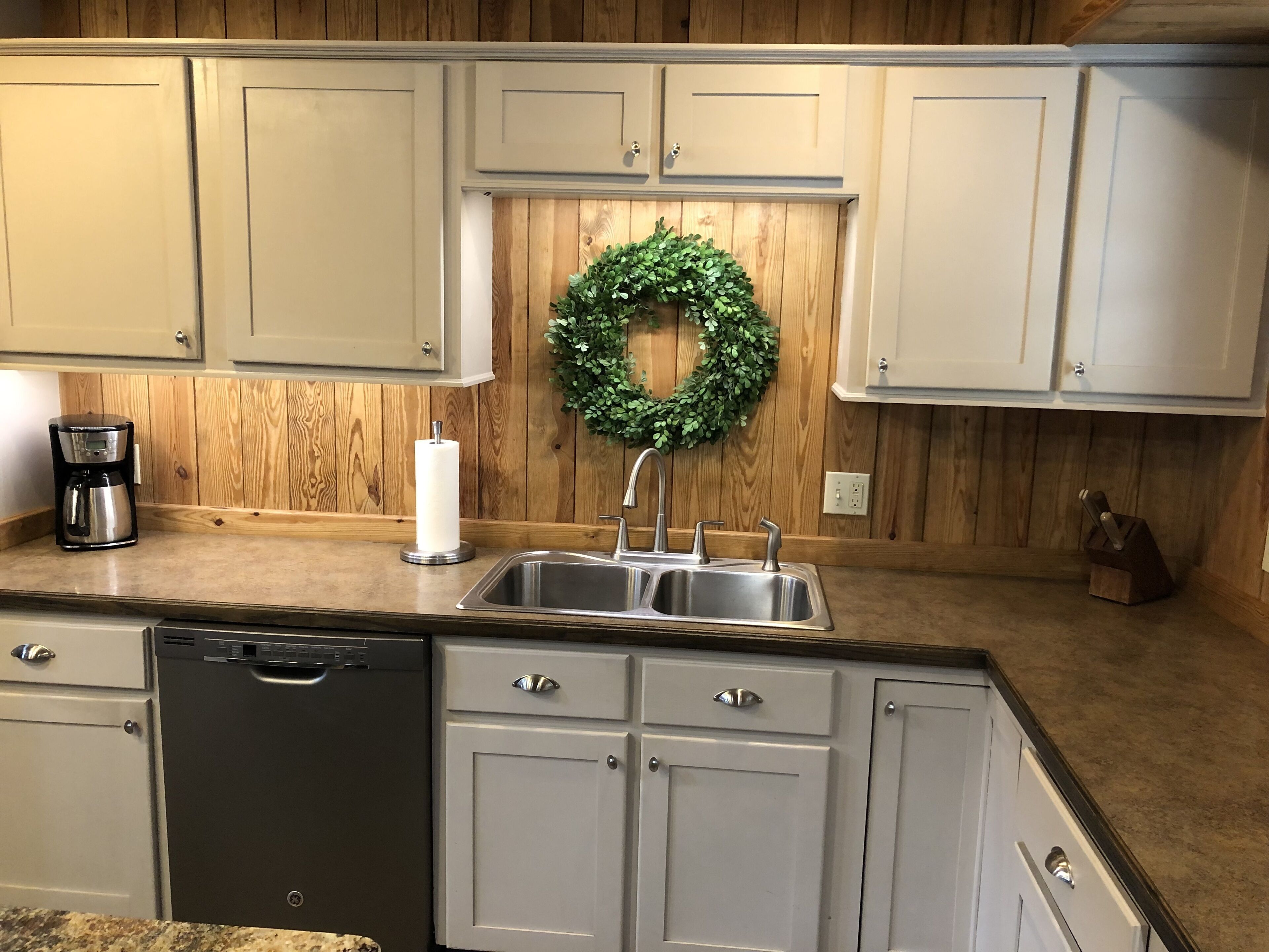 A kitchen with wooden paneling, a stainless steel sink, a coffee maker, and a dishwasher.