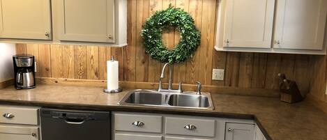 A kitchen with wooden paneling, a stainless steel sink, a coffee maker, and a dishwasher.