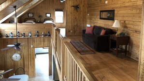 Ein gemütliches Holzhäuschen mit Schlafzimmer im Zwischengeschoss, einem Wohnbereich mit Sofa und Tisch sowie einer Essecke mit Tisch und Stühlen.