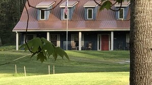 Ein zweistöckiges Haus mit rotem Dach, einer Veranda und einer Fahnenstange.