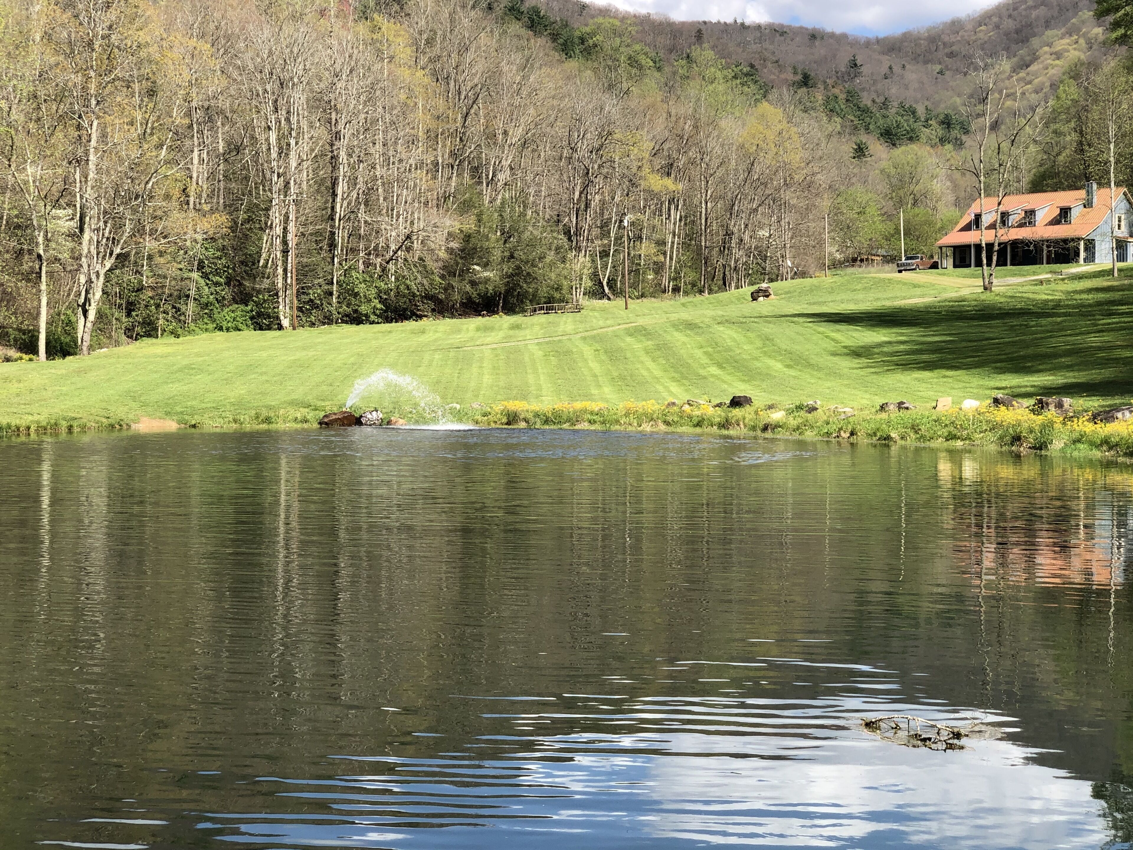 Une vue paisible sur un lac, avec une fontaine, une pelouse bien entretenue et une maison en arrière-plan.