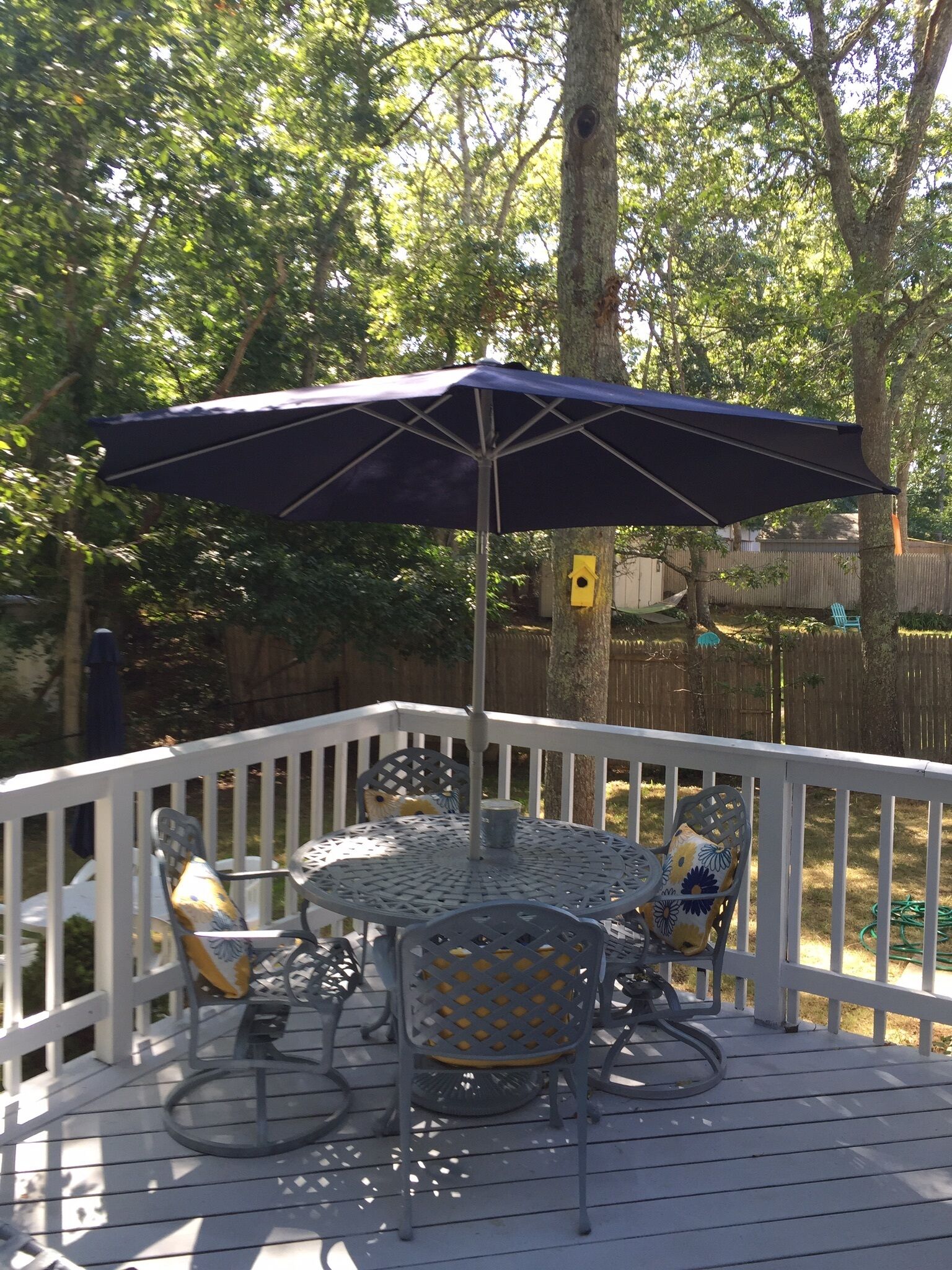 Une terrasse avec une table ronde et des chaises, un grand parasol et une rambarde blanche.