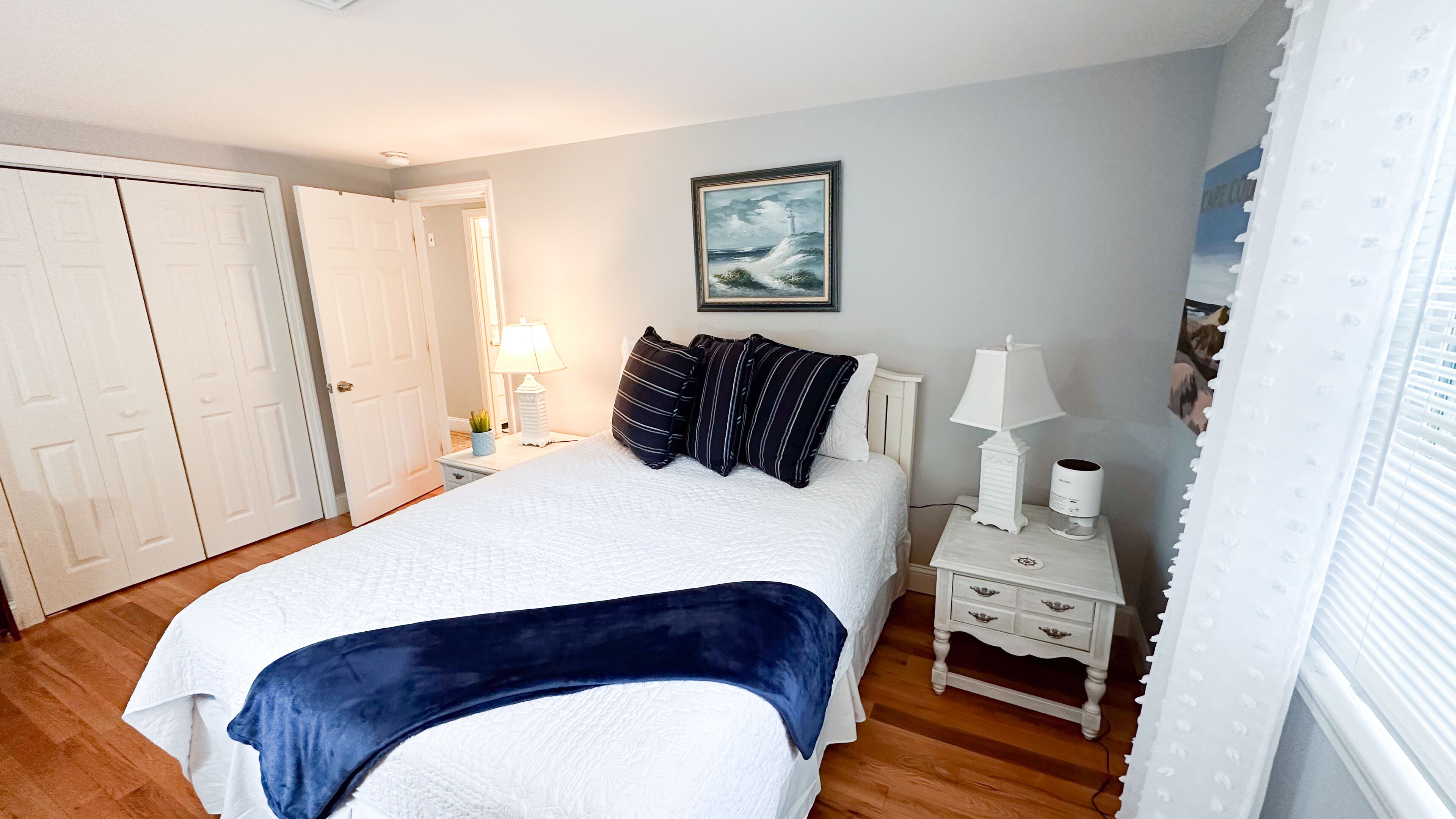 A bedroom with a bed, bedside tables, a nightstand, a lamp, a picture on the wall, and a door.