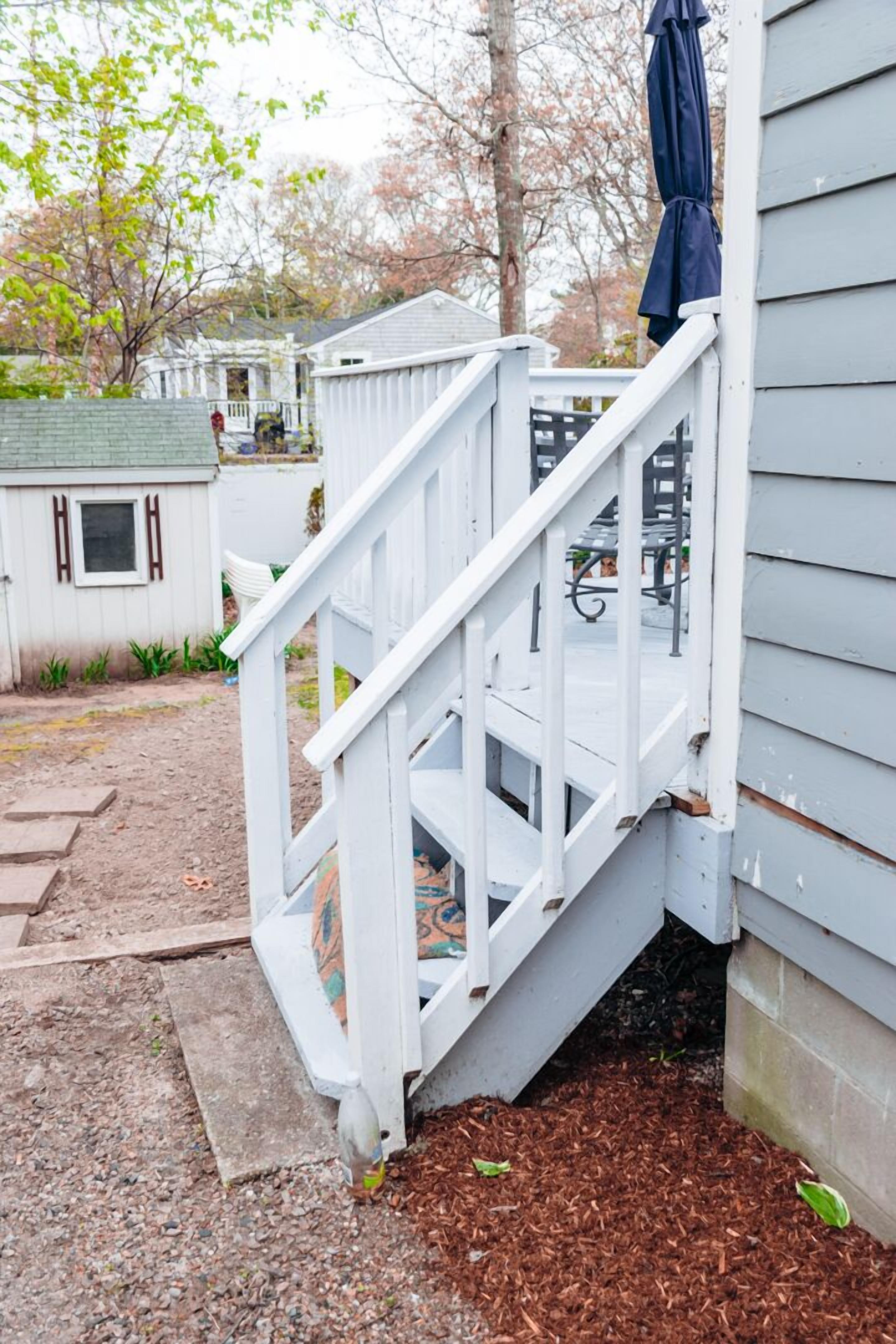 Un escalier en bois blanc mène à une véranda sur laquelle se trouve un parasol bleu.