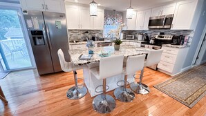 A modern kitchen with white cabinets, stainless steel appliances, and a central island with bar stools. - Quaint Cozy Beach Cape Escape (East Falmouth)