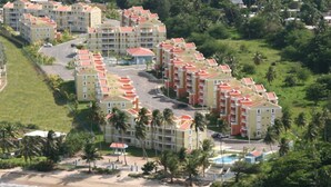 Vista aérea de un hotel costero con varias construcciones, una playa y palmeras.