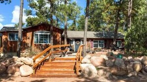 A wooden cabin with a wooden staircase leading to a porch, surrounded by large rocks and trees. - Black Forest Colorado Log Cabin (Black Forest)
