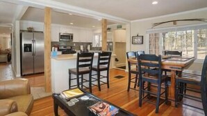A spacious living area with a wooden floor, a dining table with chairs, a kitchen area with modern appliances, and a large window providing natural light. - Black Forest Colorado Log Cabin (Black Forest)
