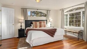 A bedroom with a large bed, two bedside tables with lamps, a window with curtains, and a wooden floor. - Black Forest Colorado Log Cabin (Black Forest)