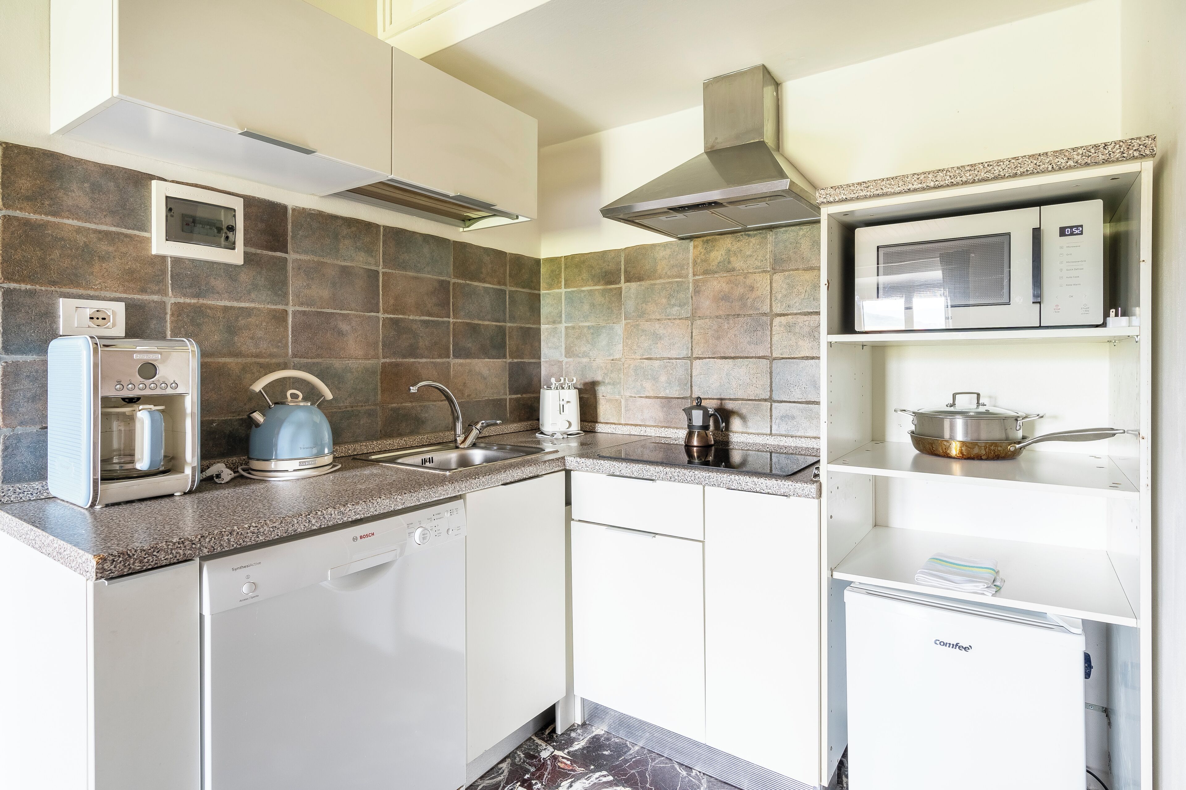 A kitchen with a Bosch dishwasher, a coffee maker, a kettle, and a microwave on a white cabinet.